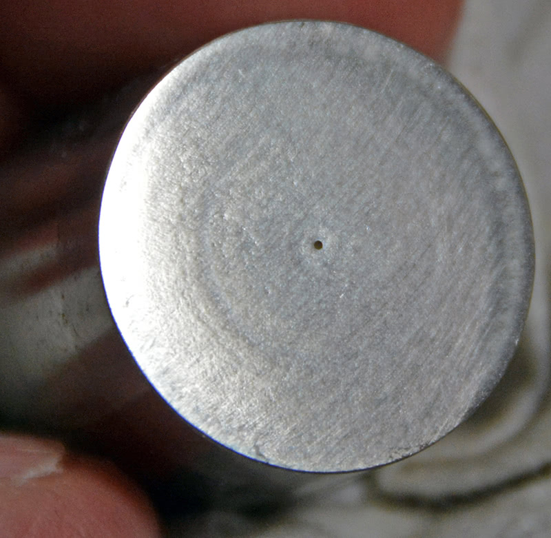 The tiny EDM hole you see is there to promote oiling between the lobe and lifter foot and slow lobe wear when running valve spring pressures that are right up near the high limit for solid lifters. Once you get to about 450 psi over the nose, you can expect to see failures. Extra oil helps. laser-or-wire-edm-hole-on-foot-promotes-cam-lobe-oiling