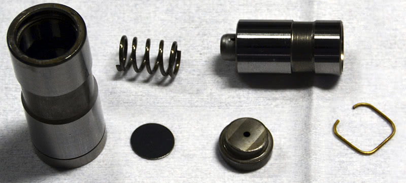 There’s not really too much to it. There’s the internal plunger, which houses the check ball and spring, the lower spring between the main body and the plunger that keeps the inner plunger pushed to the top of the bore, the oil metering disc, the pushrod set, and the retaining clip. There’s not really too much to it. There’s the internal plunger, which houses the check ball and spring, the lower spring between the main body and the plunger that keeps the inner plunger pushed to the top of the bore, the oil metering disc, the pushrod set, and the retaining clip.